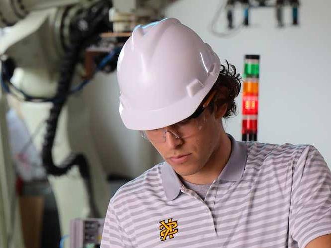 Student is wearing a hard hat with safety goggles working on a project